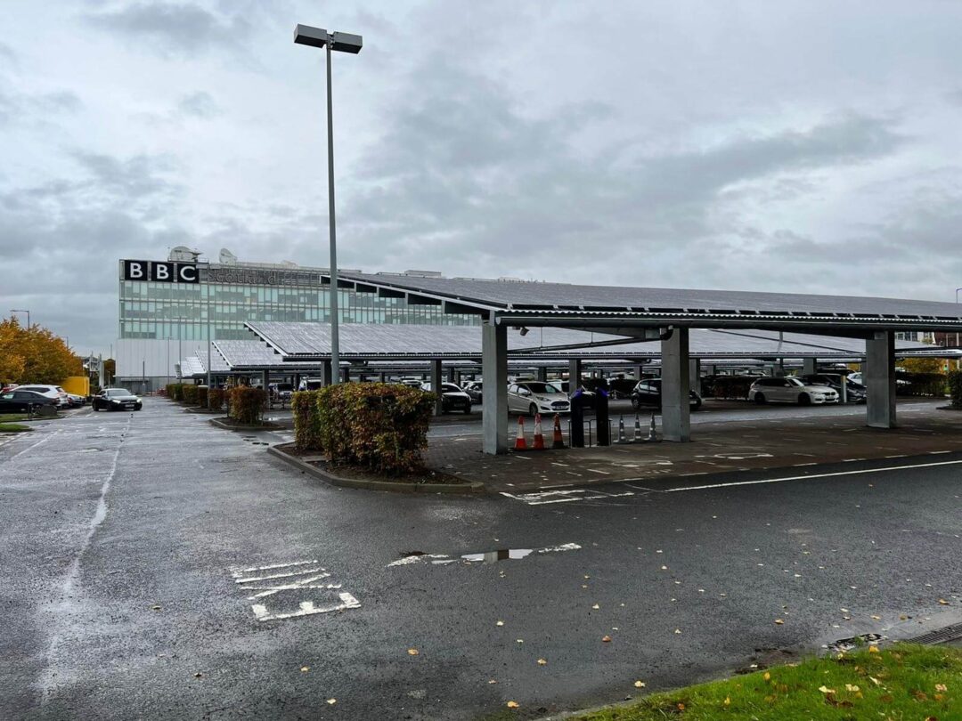 Solar carport installation in the BBC Scotland car park on a cloudy day, with multiple vehicles parked beneath the covered structures.