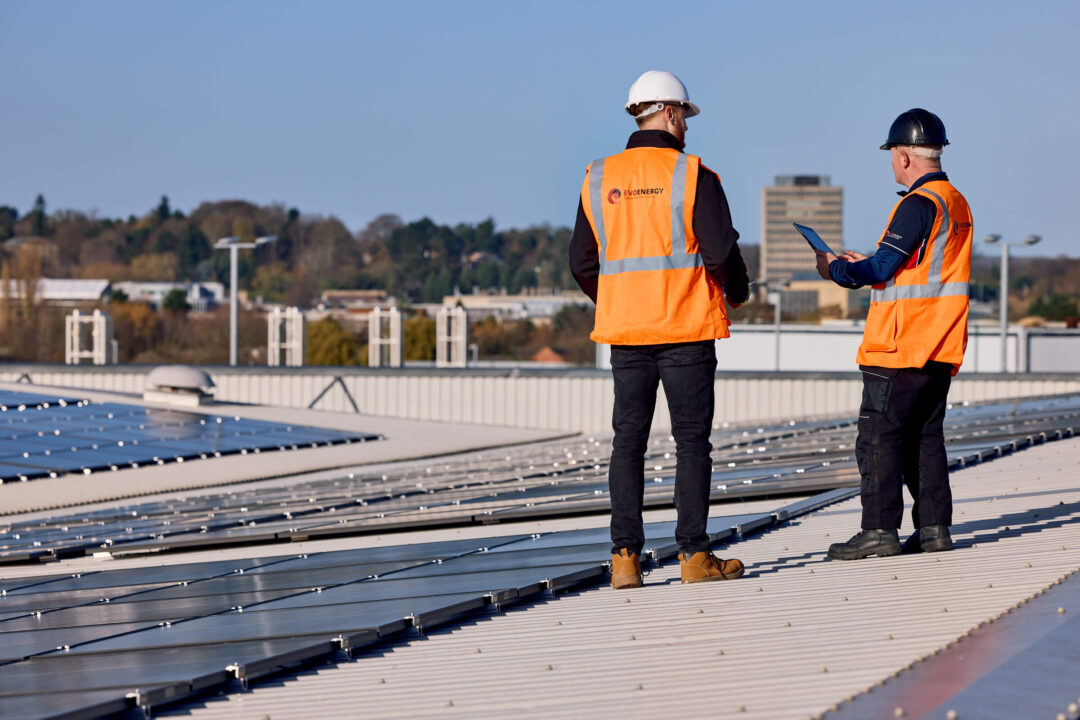 EvoEnergy engineers wearing high-visibility vests and helmets inspecting a commercial rooftop solar installation.
