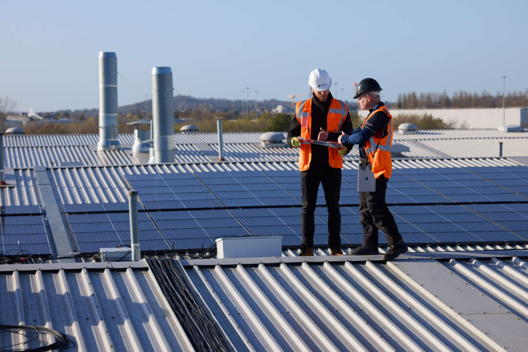 Two EvoEnergy engineers reviewing plans on a rooftop overlooking a large commercial solar panel installation.