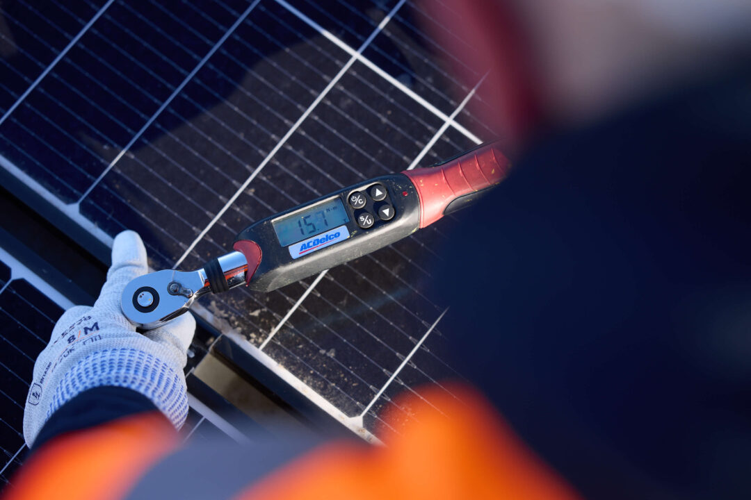 Engineer using a digital torque wrench to secure a bolt on a solar panel frame during installation."
