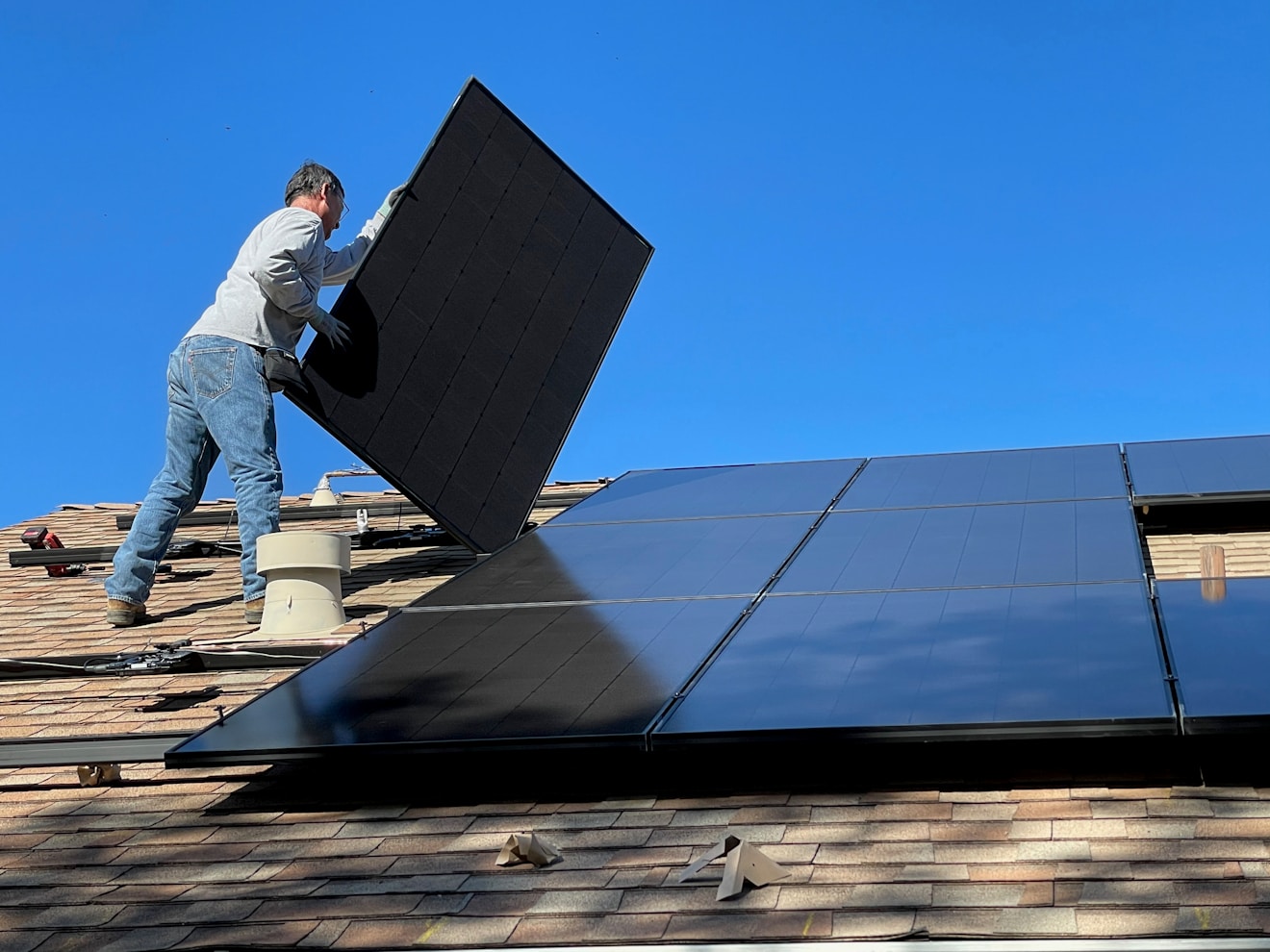 Installer lifting a solar panel into place on a residential rooftop during a solar PV installation on a clear sunny day in Solar Rooftop