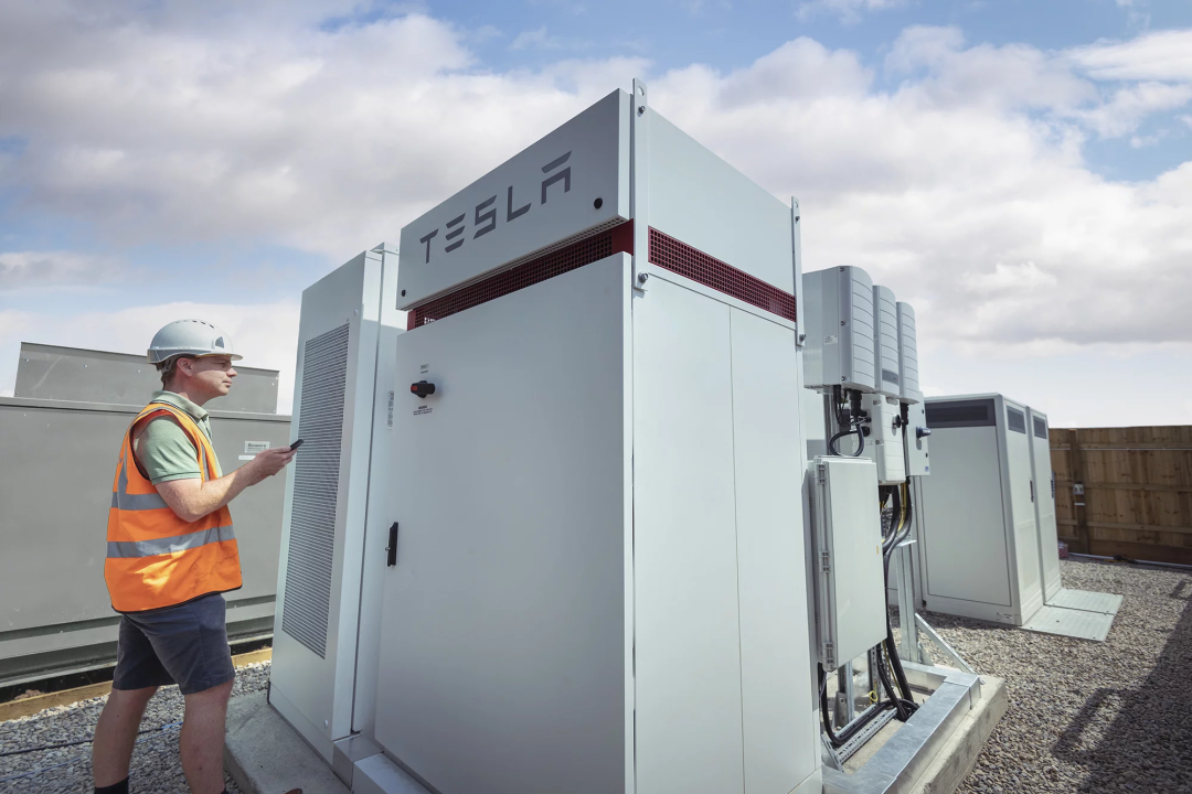 An engineer inspecting a Tesla commercial battery storage unit installed on an outdoor energy site.