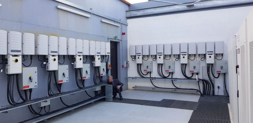Engineer inspecting a commercial solar PV inverter room with multiple wall-mounted inverters and electrical isolation switches.