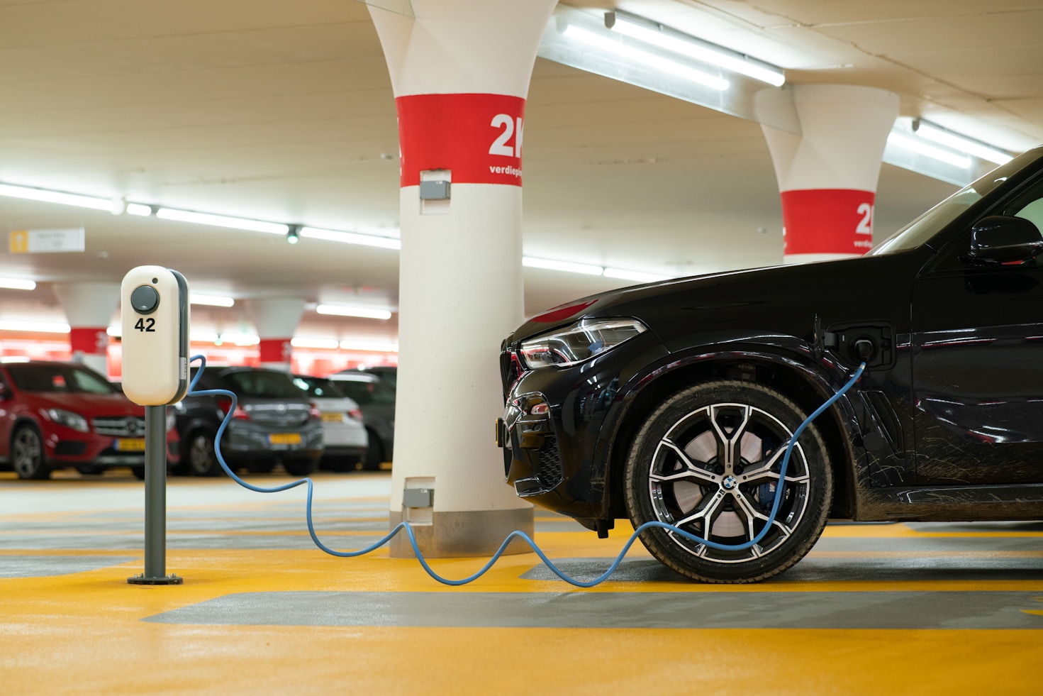 Electric vehicle charging at an indoor car park EV charging station, with a blue cable connected to a black car.