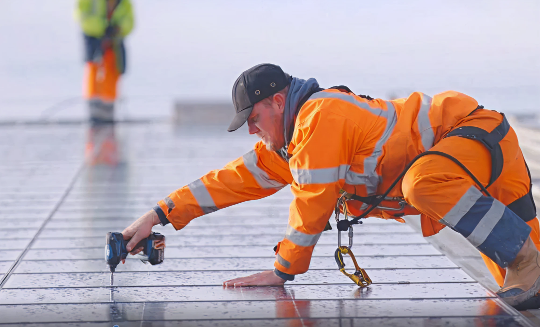 Engineer in high-visibility safety gear installing solar panels with a power drill while secured with a fall-arrest harness in Repowering/Upgrade
