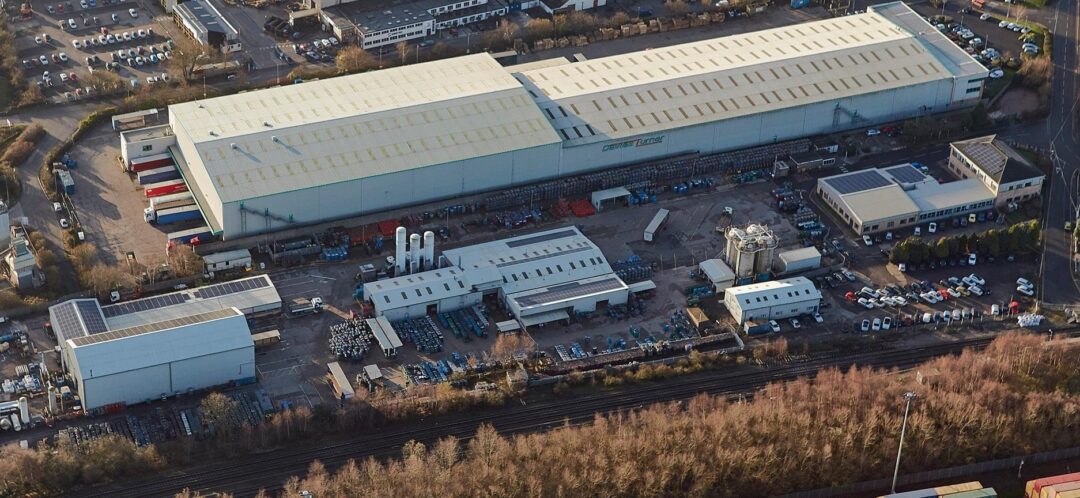 Aerial view of a large industrial site with warehouses, production facilities, storage yards, and adjacent car parks.
