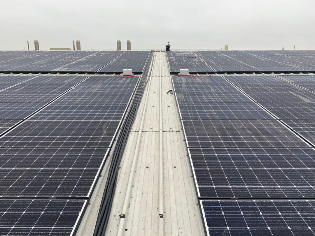 Close-up view of rooftop solar panels installed on a large industrial metal roof under an overcast sky.