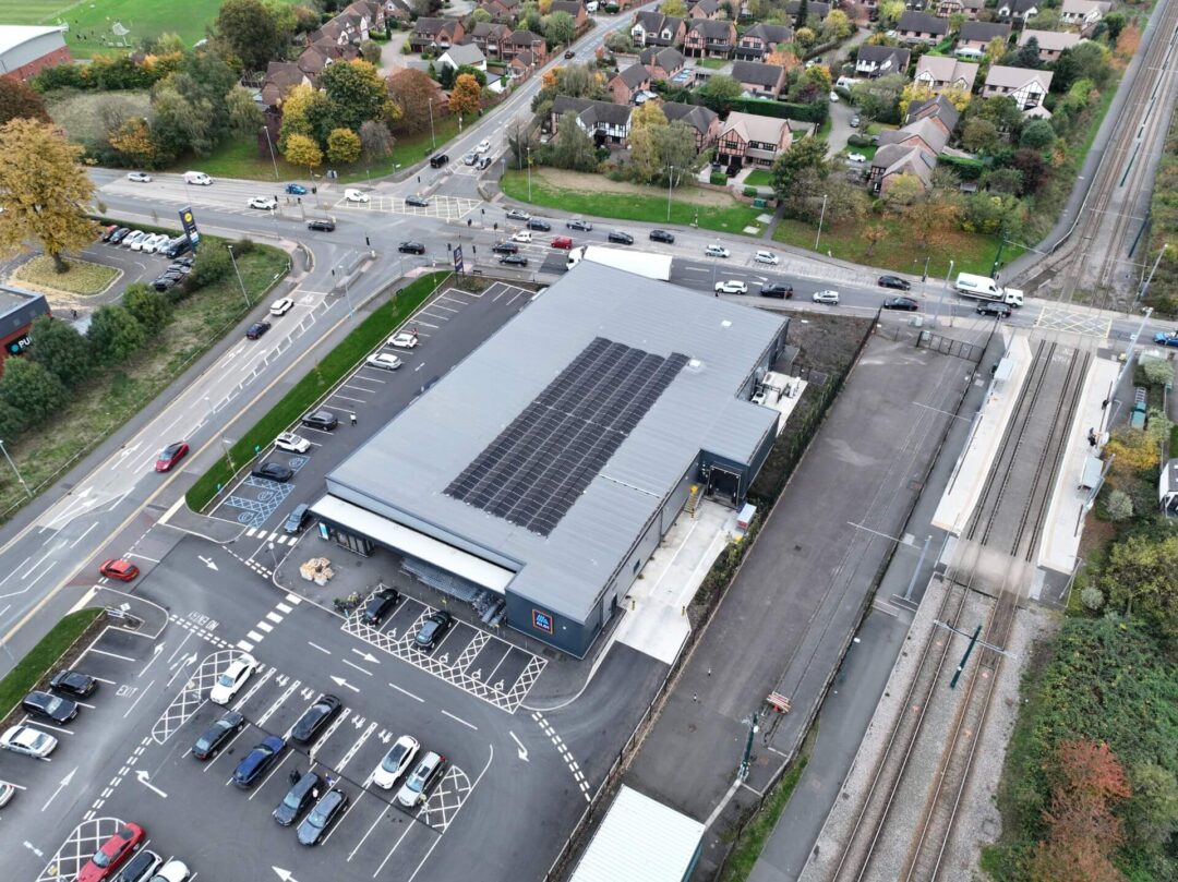 Aerial view of a supermarket with rooftop solar panels, adjacent to a tram station and surrounded by roads and residential housing in Aldi Stores