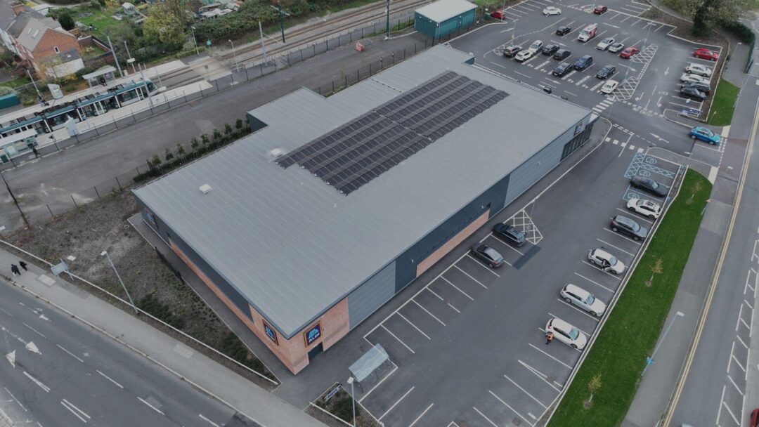 Aerial view of an Aldi supermarket with rooftop solar panels, adjacent to a tram station and surrounded by a car park in Alsdi Stores