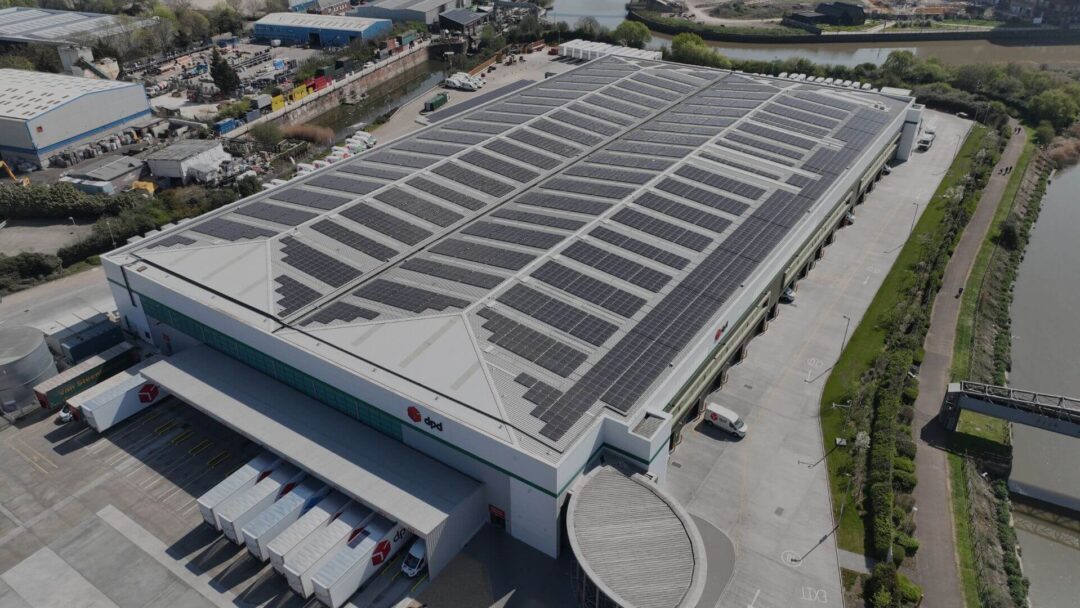 Aerial view of a DPD logistics warehouse with a large-scale rooftop solar PV system installed, situated next to a river and pedestrian walkway for sustainable operations in DPD Docklands.