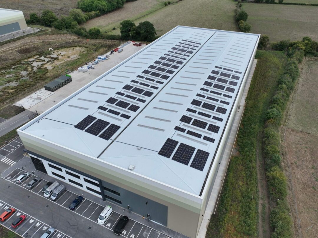 modern commercial or logistics building, viewed aerially, with two distinct PV arrays and a large marked employee parking lot in Furniture Box