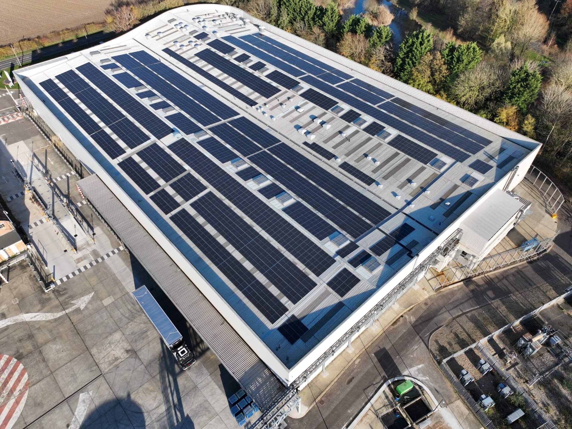 Aerial photo of a large logistics facility with a full-roof solar PV system, surrounded by trees and adjacent to an HGV loading area with one articulated lorry parked at a bay in GCB Cocoa UK