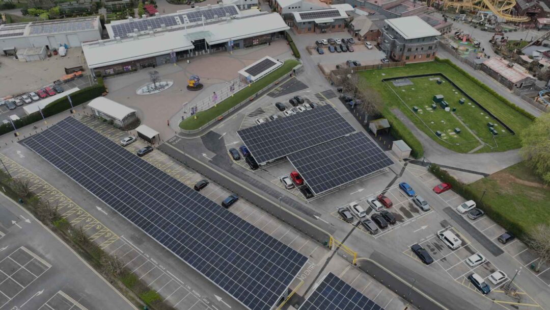 Aerial view of solar carports and rooftop solar panels installed at a theme park entrance, with EV parking bays and visitor drop-off zones integrated into the renewable energy system in Paultons Park