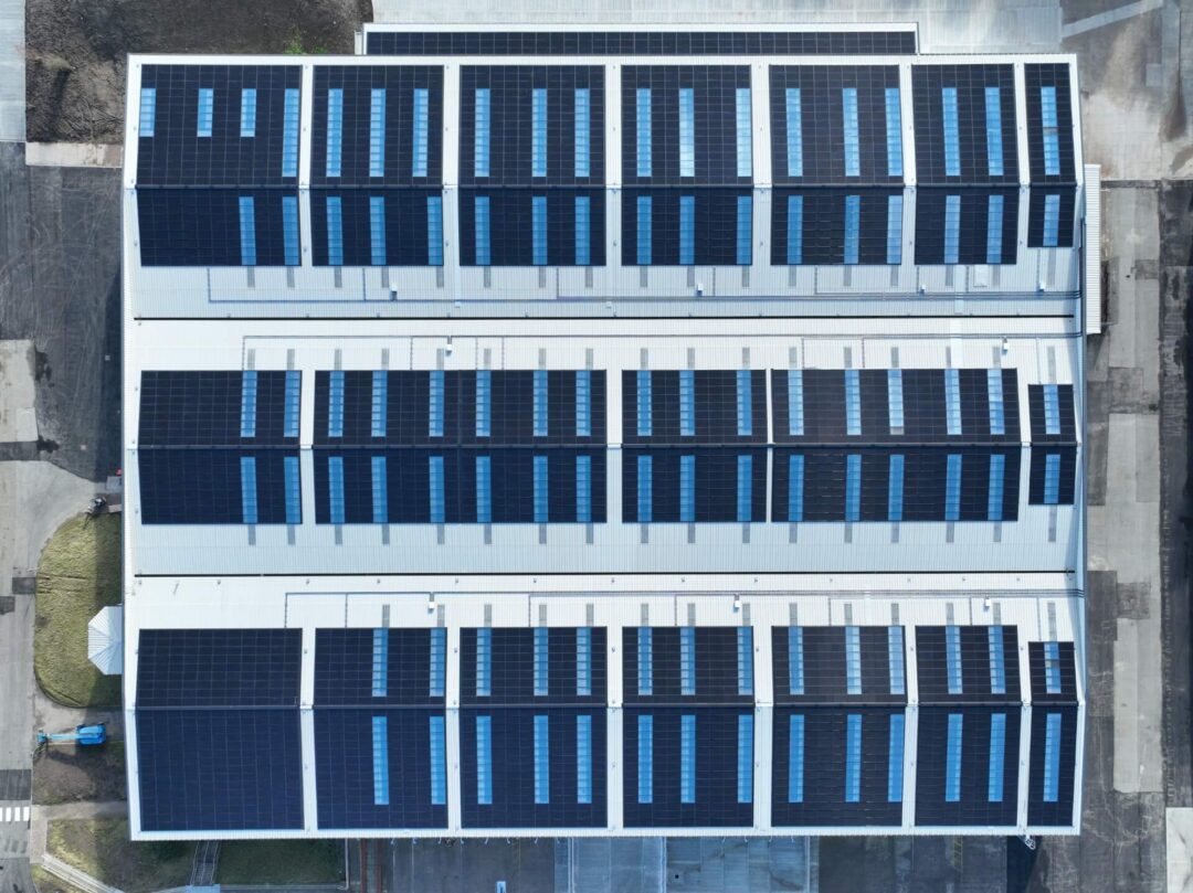 Top-down aerial view of a large industrial rooftop covered with multiple rows of solar panels installed in uniform sections across the white in Rainhill Road.