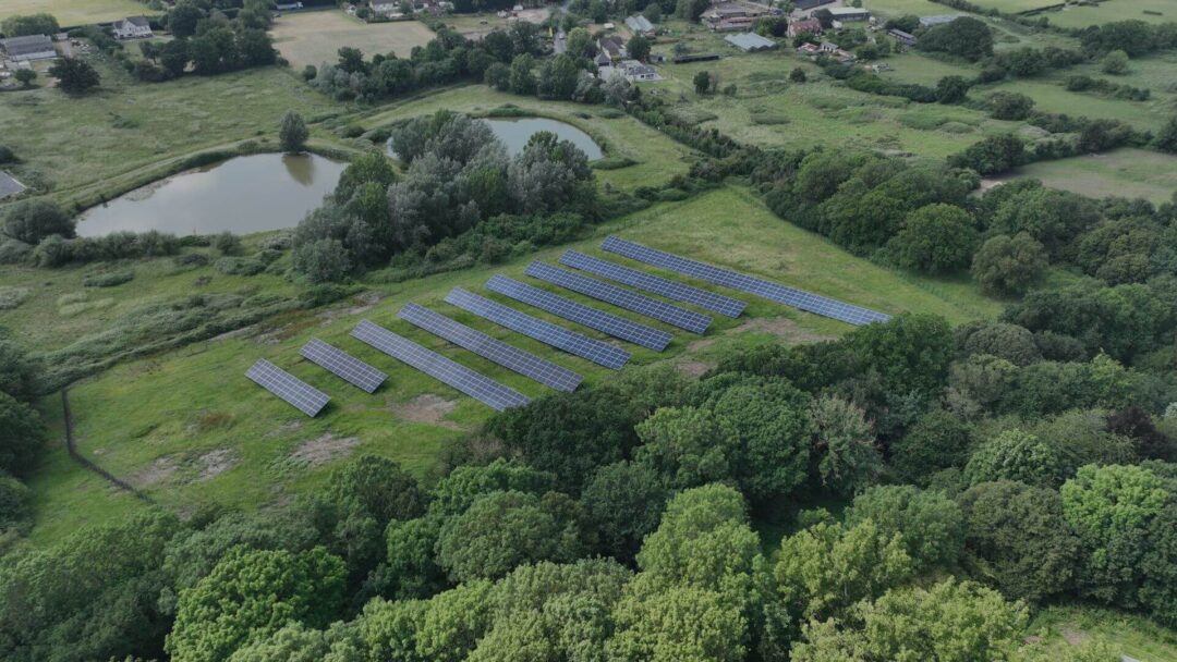 Aerial view of a small ground-mounted solar farm nestled within a rural landscape, surrounded by trees, ponds, and countryside properties, generating clean energy in Scouts