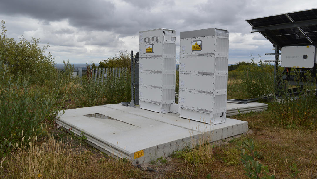Outdoor battery storage units supporting the Brymbo solar installation beside ground-mounted solar panels under cloudy skies.