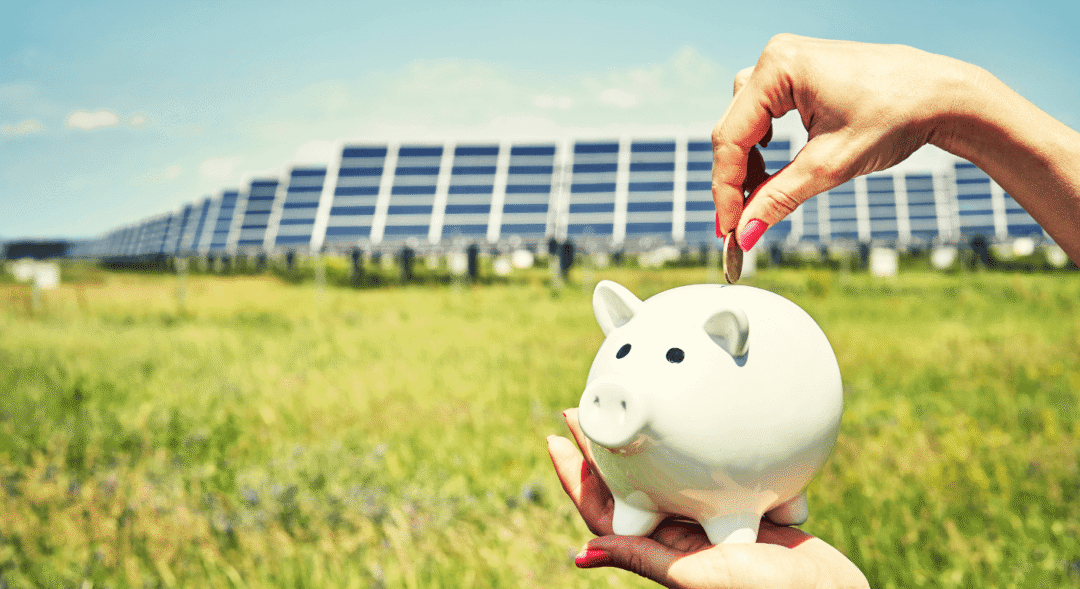 Coin placed into piggy bank beside solar farm, illustrating investment returns and solar project bankability.