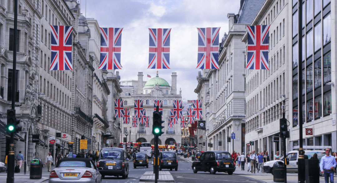 Union Jack flags hang above Regent Street in central London, with traffic and pedestrians beneath.